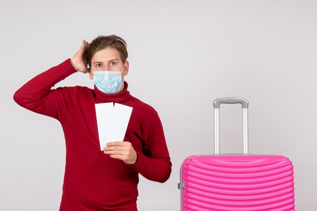 Vorderansicht des jungen Mannes in der Maske, die Karten an der weißen Wand hält