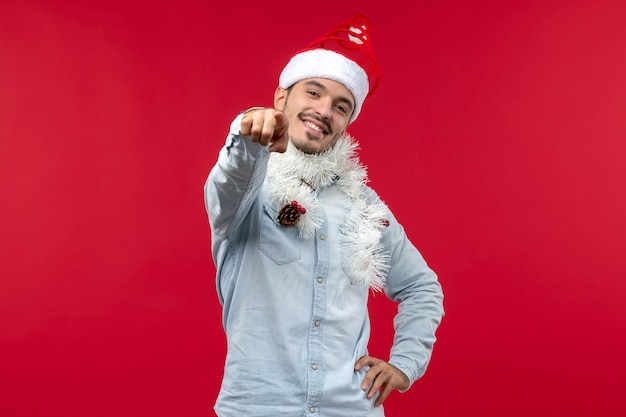 Kostenloses Foto vorderansicht des jungen mannes in der weihnachtsstimmung, die auf rote wand lächelt