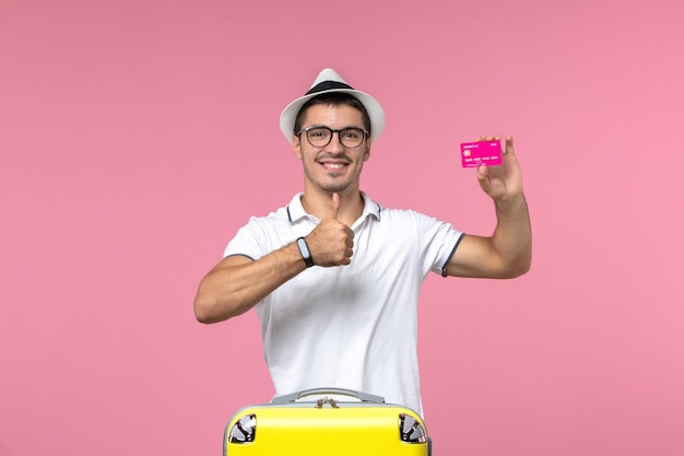 Vorderansicht des jungen Mannes mit Bankkarte im Sommerurlaub an der rosa Wand