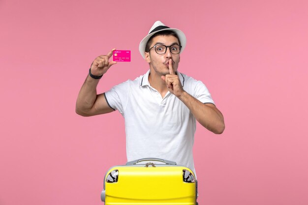 Vorderansicht des jungen Mannes mit Bankkarte im Sommerurlaub an der rosa Wand