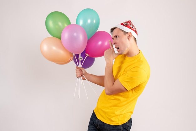 Vorderansicht des jungen Mannes mit bunten Luftballons auf weißer Wand