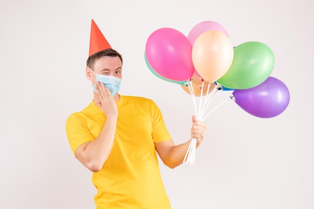 Vorderansicht des jungen Mannes mit bunten Luftballons auf weißer Wand