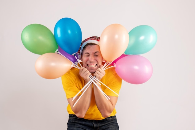 Vorderansicht des jungen Mannes mit bunten Luftballons auf weißer Wand