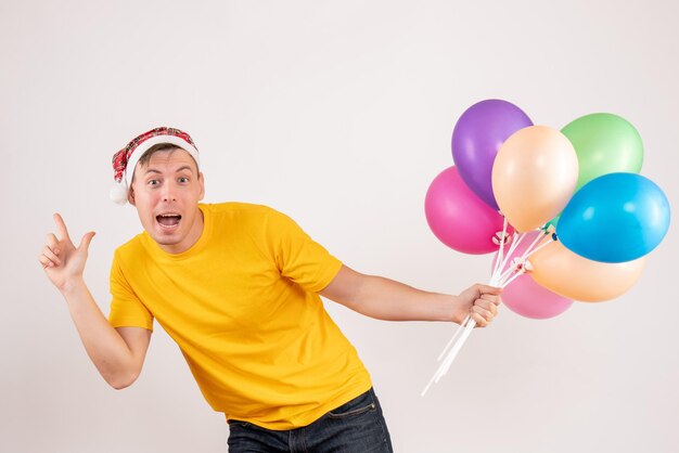 Vorderansicht des jungen Mannes mit bunten Luftballons auf weißer Wand