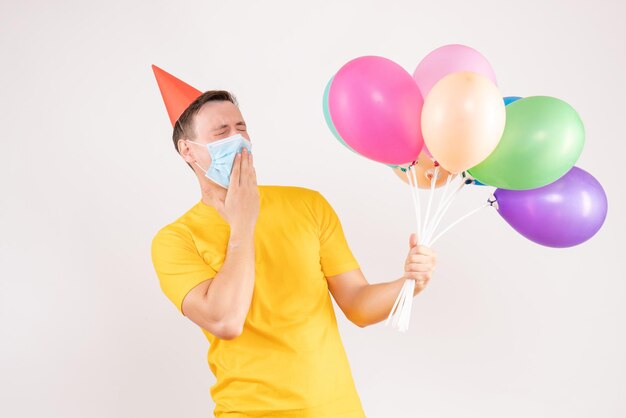 Vorderansicht des jungen Mannes mit bunten Luftballons auf weißer Wand