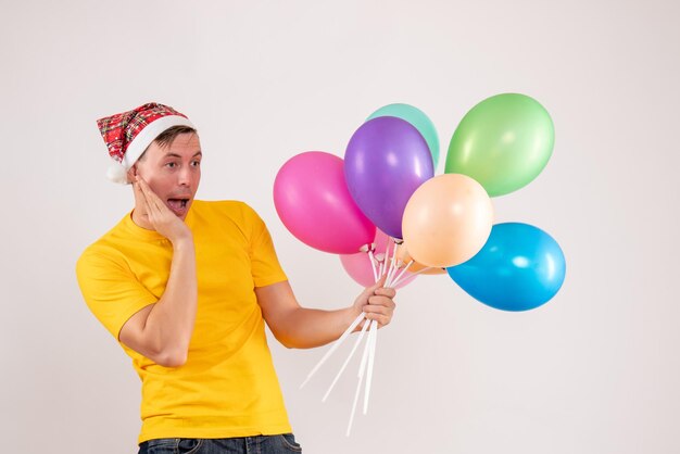 Vorderansicht des jungen Mannes mit bunten Luftballons auf weißer Wand