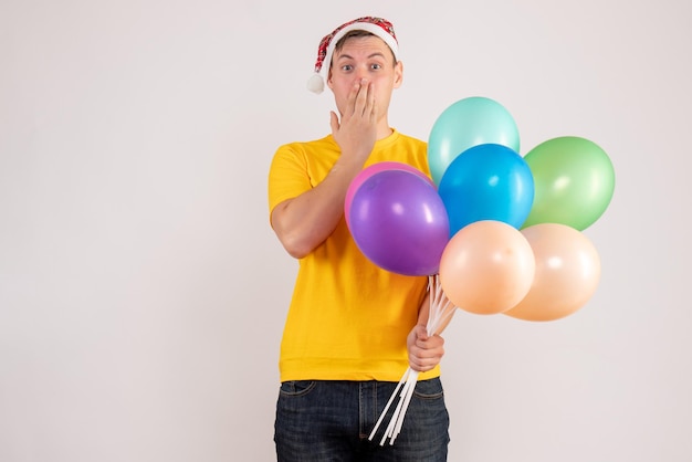 Vorderansicht des jungen Mannes mit bunten Luftballons auf weißer Wand