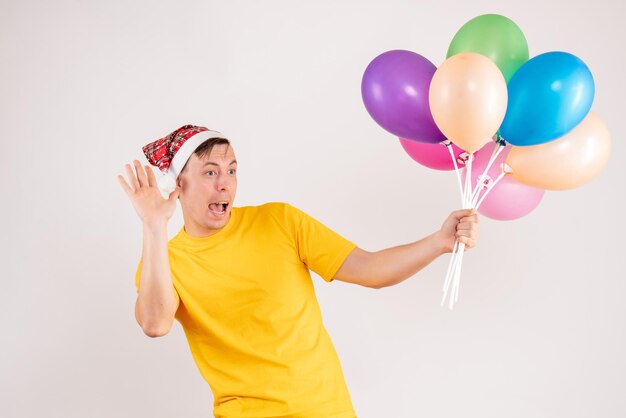 Vorderansicht des jungen Mannes mit bunten Luftballons auf weißer Wand