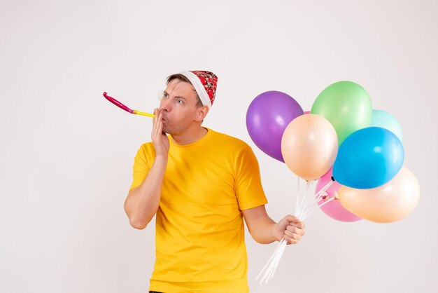 Vorderansicht des jungen Mannes mit bunten Luftballons auf weißer Wand
