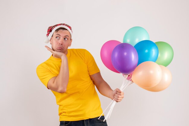 Vorderansicht des jungen mannes mit bunten luftballons auf weißer wand