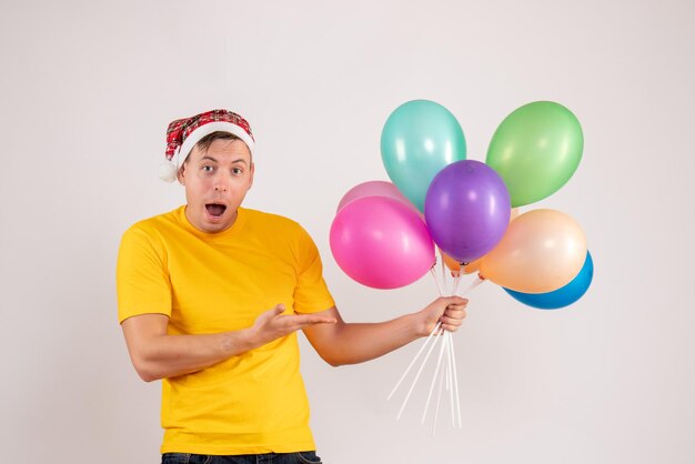 Vorderansicht des jungen Mannes mit bunten Luftballons auf weißer Wand