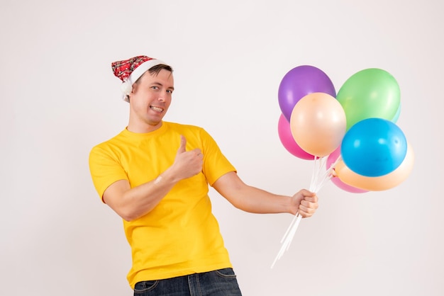 Vorderansicht des jungen Mannes mit bunten Luftballons auf weißer Wand