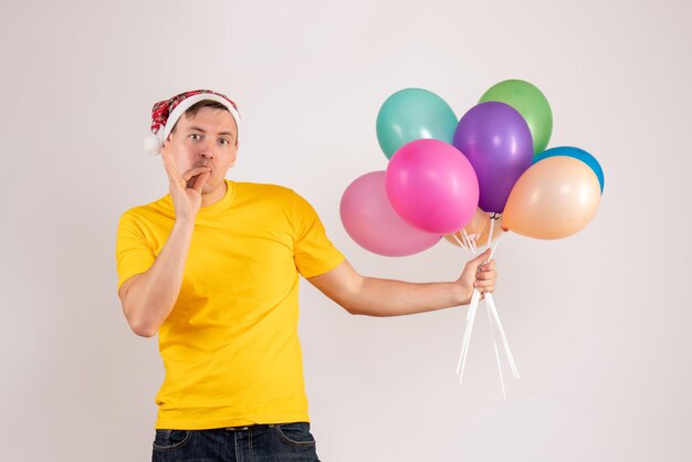 Vorderansicht des jungen Mannes mit bunten Luftballons auf weißer Wand