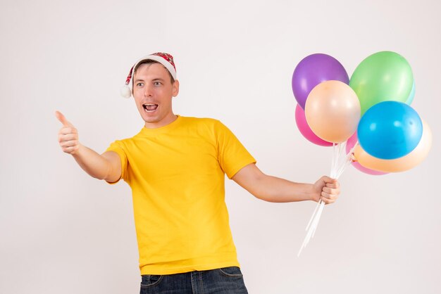 Vorderansicht des jungen Mannes mit bunten Luftballons auf weißer Wand