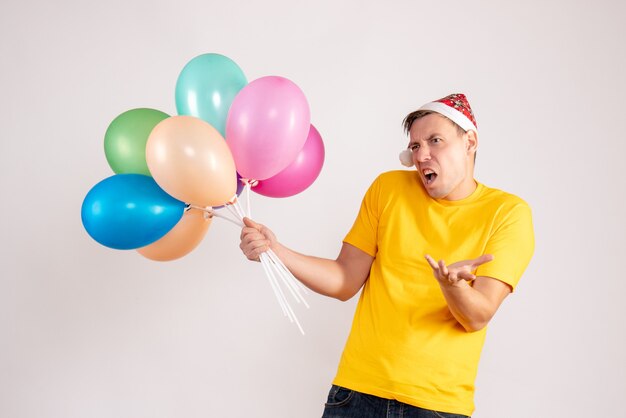 Vorderansicht des jungen Mannes mit bunten Luftballons auf weißer Wand