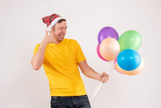 Vorderansicht des jungen Mannes mit bunten Luftballons auf weißer Wand