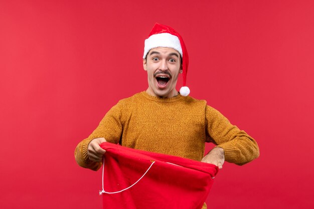 Vorderansicht des jungen mannes mit der gegenwärtigen tasche an der roten wand