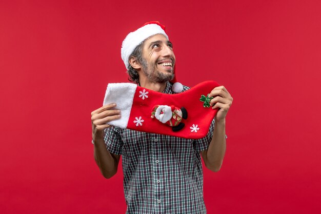 Vorderansicht des jungen Mannes mit der großen Weihnachtssocke an der roten Wand