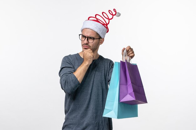 Vorderansicht des jungen Mannes mit Geschenken nach dem Einkaufen an der weißen Wand