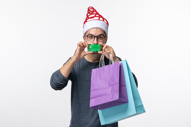 Vorderansicht des jungen mannes mit geschenken und bankkarte auf weißer wand