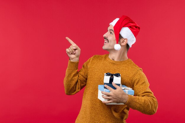 Vorderansicht des jungen Mannes mit Neujahrsgeschenken an der roten Wand