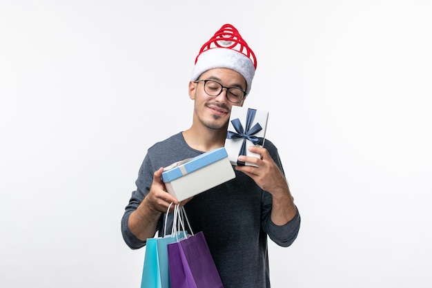 Vorderansicht des jungen Mannes mit Paketen und Geschenken auf weißer Wand