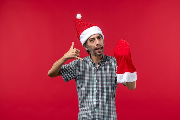 Kostenloses Foto vorderansicht des jungen mannes mit roter weihnachtsmütze an der roten wand