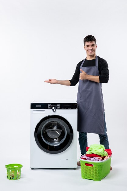 Vorderansicht des jungen Mannes mit schmutziger Kleidung und Waschmaschine auf weißer Wand