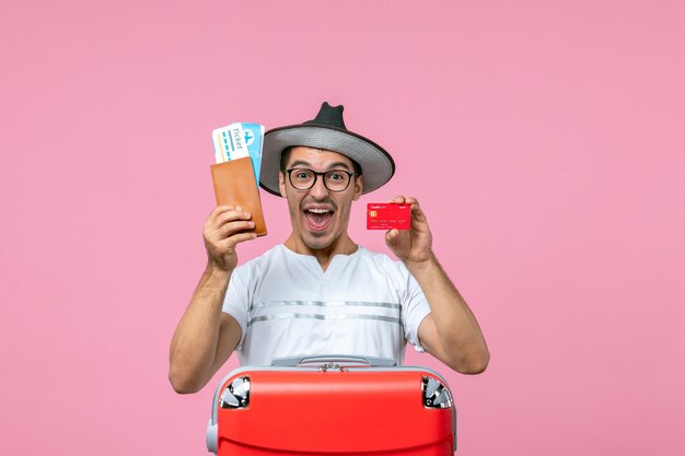 Vorderansicht des jungen Mannes mit Tickets und Bankkarte an der rosa Wand