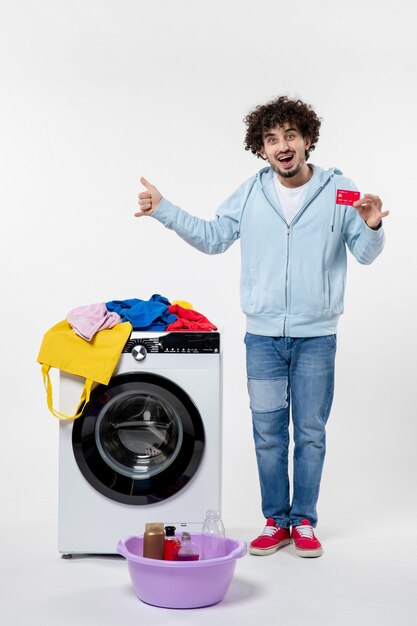 Vorderansicht des jungen Mannes mit Waschmaschine mit Bankkarte auf weißer Wand