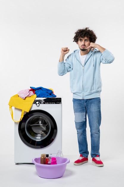 Kostenloses Foto vorderansicht des jungen mannes mit waschmaschine und schmutziger kleidung auf weißer wand