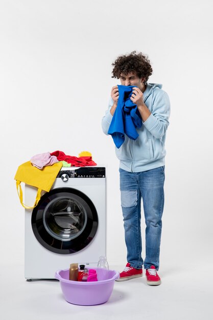 Kostenloses Foto vorderansicht des jungen mannes mit waschmaschine und schmutziger kleidung auf weißer wand