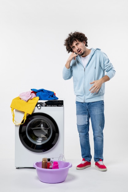 Kostenloses Foto vorderansicht des jungen mannes mit waschmaschine und schmutziger kleidung auf weißer wand