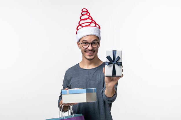 Vorderansicht des jungen Mannes mit Weihnachtsgeschenken an der weißen Wand