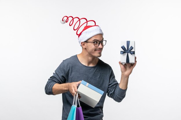 Vorderansicht des jungen Mannes mit Weihnachtsgeschenken an der weißen Wand