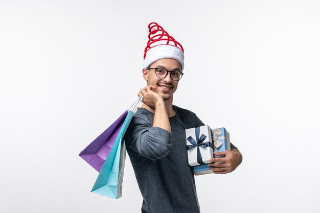 Vorderansicht des jungen Mannes mit Weihnachtsgeschenken an der weißen Wand