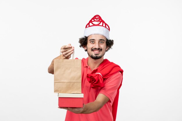 Vorderansicht des jungen Mannes mit Weihnachtsgeschenken an der weißen Wand