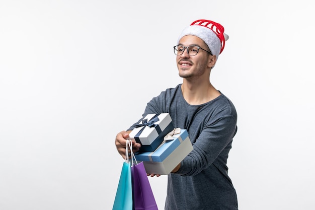 Vorderansicht des jungen Mannes mit Weihnachtsgeschenken auf weißer Wand