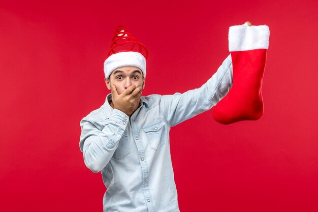 Vorderansicht des jungen Mannes mit Weihnachtssocke auf roter Wand