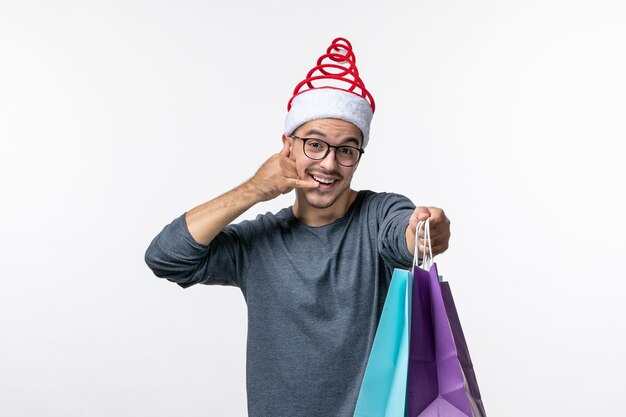 Vorderansicht des jungen Mannes nach dem Weihnachtseinkauf an der weißen Wand