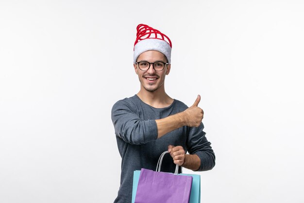 Vorderansicht des jungen Mannes nach dem Weihnachtseinkauf an der weißen Wand