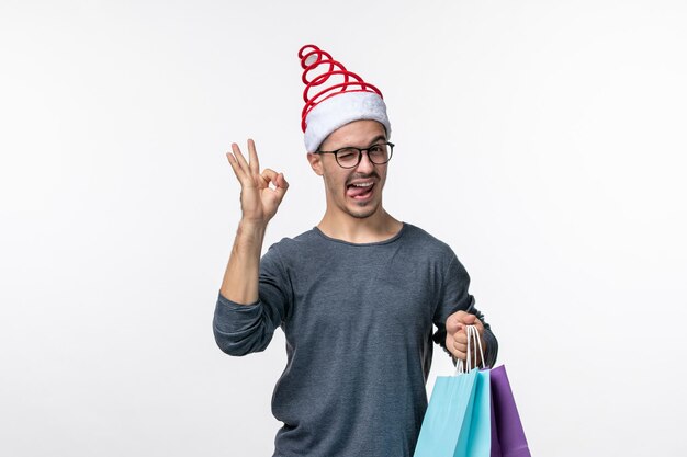 Vorderansicht des jungen Mannes nach dem Weihnachtseinkauf an der weißen Wand