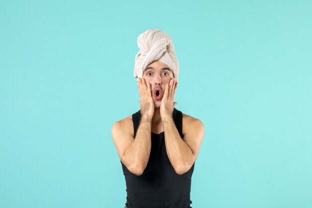 Vorderansicht des jungen Mannes nach der Dusche mit Handtuch auf dem Kopf an blauer Wand