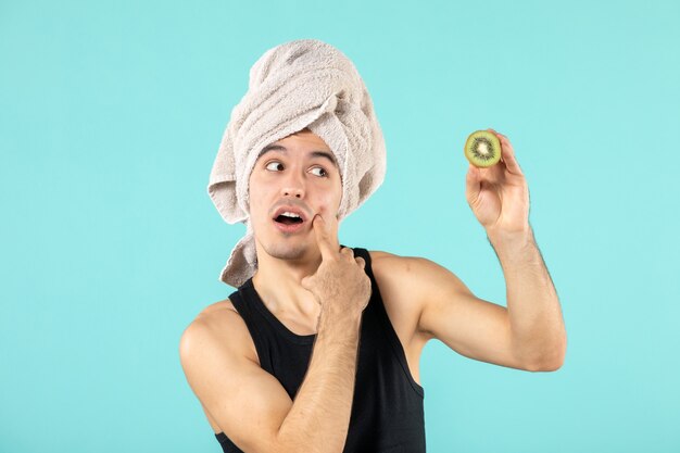Vorderansicht des jungen Mannes nach der Dusche mit Kiwischeiben an blauer Wand