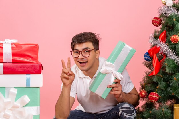 Vorderansicht des jungen Mannes um Geschenke und Weihnachtsbaum an der rosa Wand