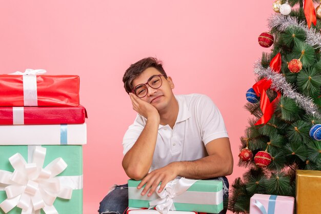 Vorderansicht des jungen Mannes um Geschenke und Weihnachtsbaum an der rosa Wand