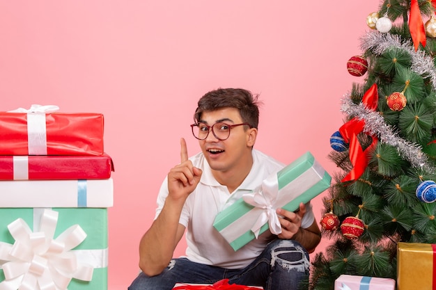 Vorderansicht des jungen Mannes um Geschenke und Weihnachtsbaum an der rosa Wand