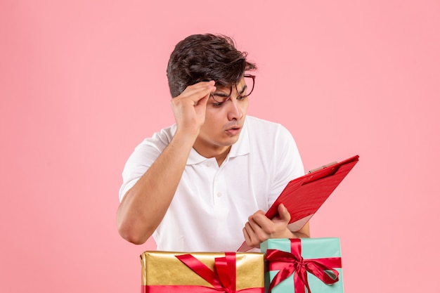 Vorderansicht des jungen Mannes um Weihnachten präsentiert das Halten der Aktennotiz an der rosa Wand