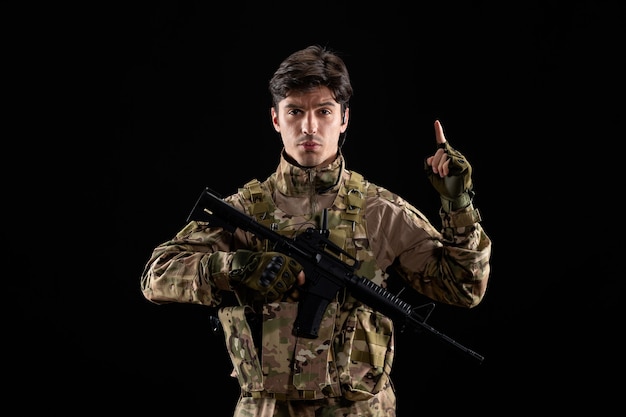 Vorderansicht des jungen Soldaten in Uniform mit Gewehr auf schwarzer Wand