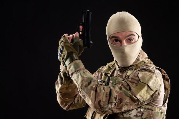 Vorderansicht des jungen Soldaten in Uniform mit Pistole an der schwarzen Wand
